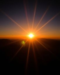 This is an intense photograph of a sunset from a high alpine peak, dominated by pure, jet black tones and deep shadows. The d