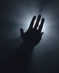 A captivating and ethereal image depicting a hand reaching towards a hazy light emerging from darkness, bathed in soft light.