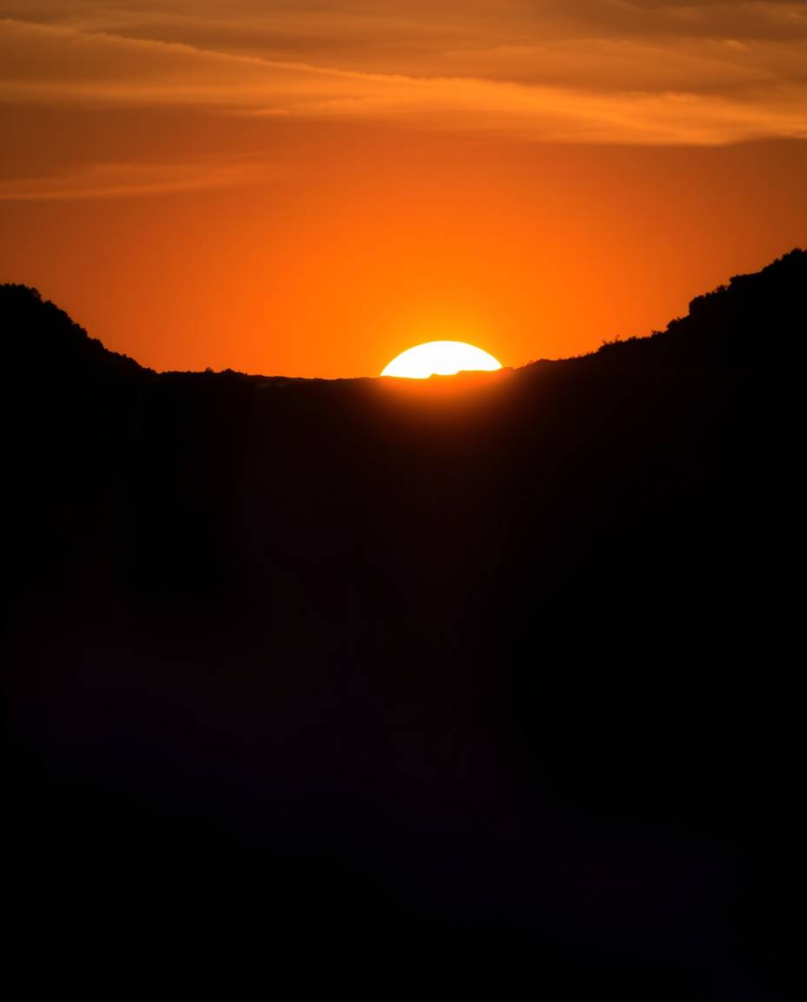 A silhouetted backlighting long exposure photograph captures a sun setting behind a dramatic waterfall. The image features pr