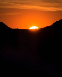 A silhouetted backlighting long exposure photograph captures a sun setting behind a dramatic waterfall. The image features pr