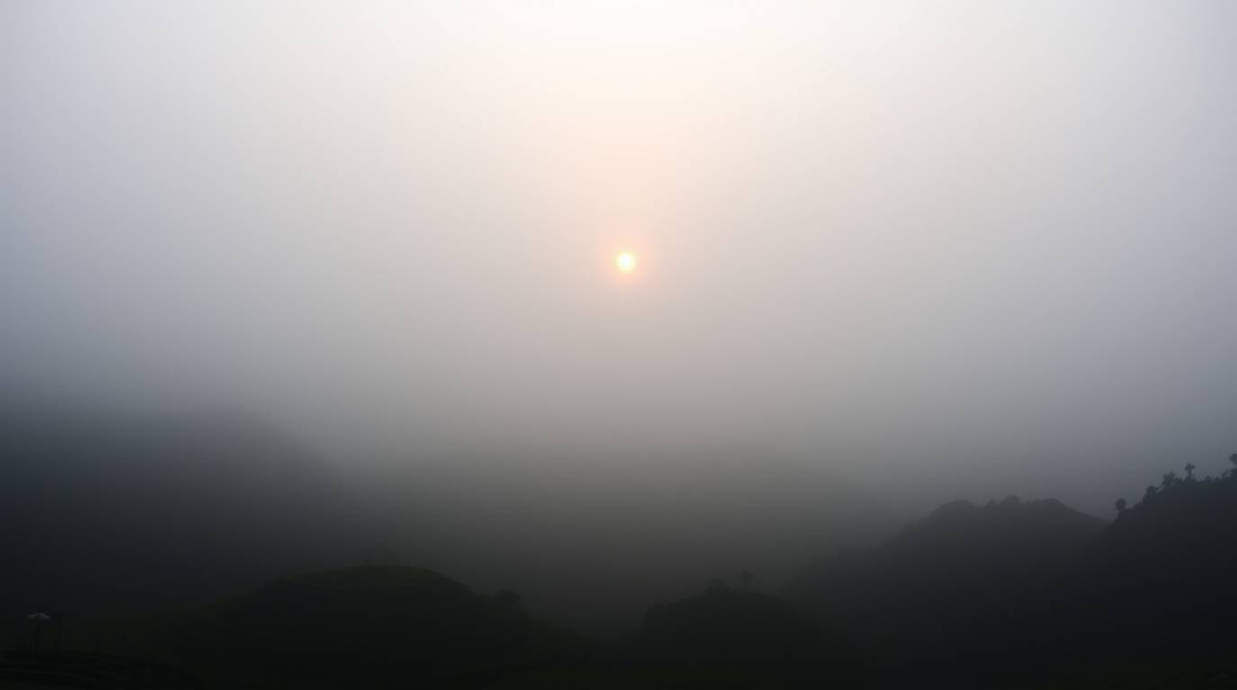 A moody style photograph capturing a sunset over breathtaking mountainous rice terraces shrouded in thick fog. Low visibility