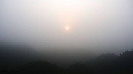 A moody style photograph capturing a sunset over breathtaking mountainous rice terraces shrouded in thick fog. Low visibility