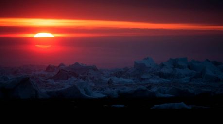 A high-contrast, low-key photograph capturing the breathtaking beauty of a sunset over icy polar glaciers. The intense jet bl