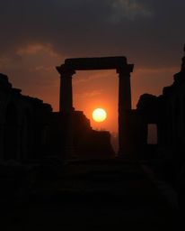 A moody, mystic, and enchanting scene depicts a sunset casting shadows through ancient stone ruins. The style features low co