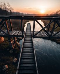 This is a high-angle photograph of an old wooden bridge over a river at sunset, captured from a high, elevated viewpoint. The
