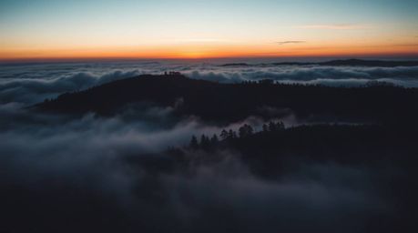 A breathtaking cinematic image captures fog-covered hills bathed in the warm glow of a setting sun.  The scene is dramaticall