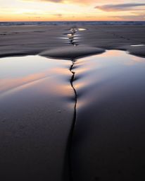 A distinct split, tight close-up shot captures a sunset sky mirrored in tidal pools on a beach. The composition is characteri