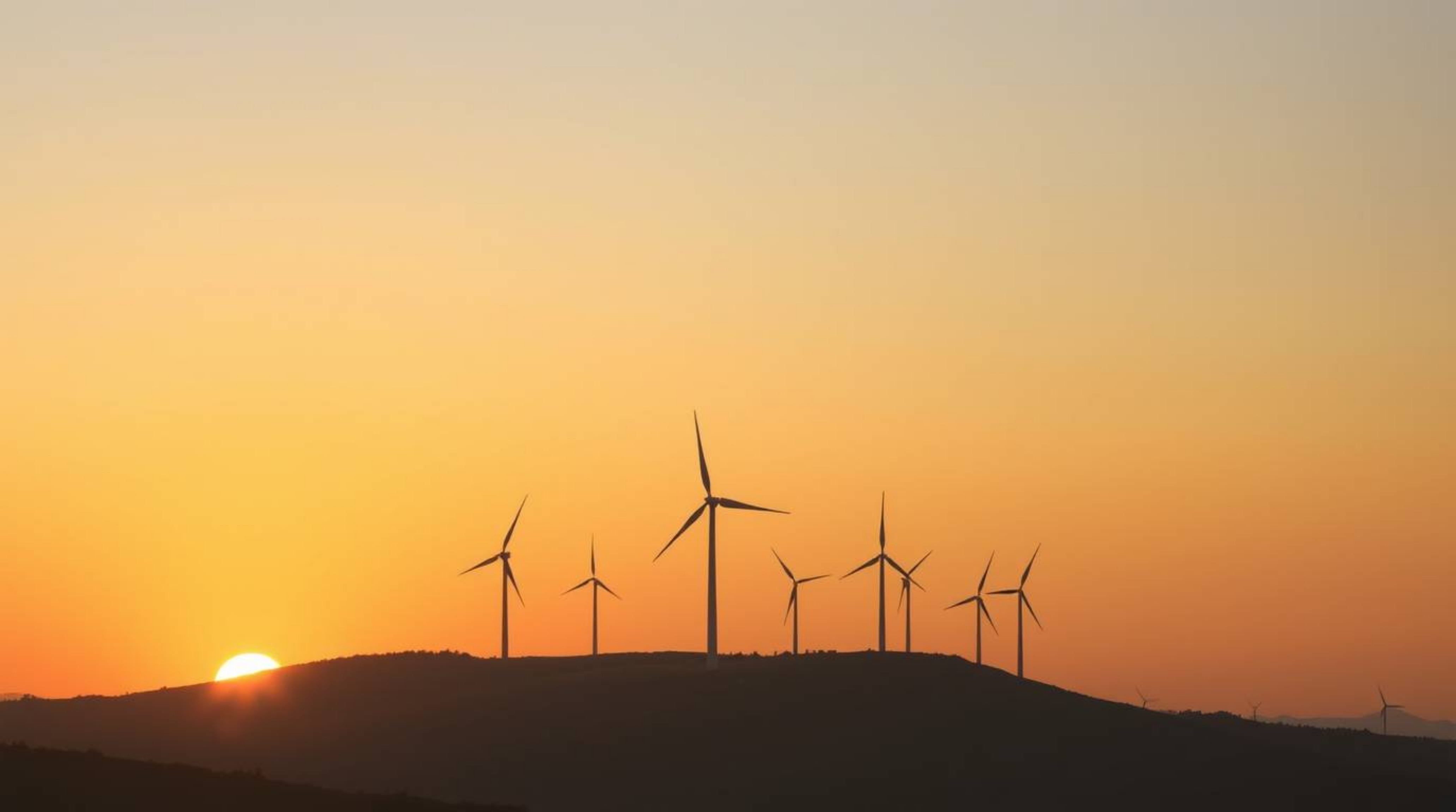 A dreamy atmosphere is captured in this stunning image of a smooth gradient sunset behind wind turbines perched on a hill.  T