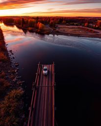 An overhead bird's-eye view of an old wooden bridge spanning a river at sunset. This image is characterized by its vivid elec