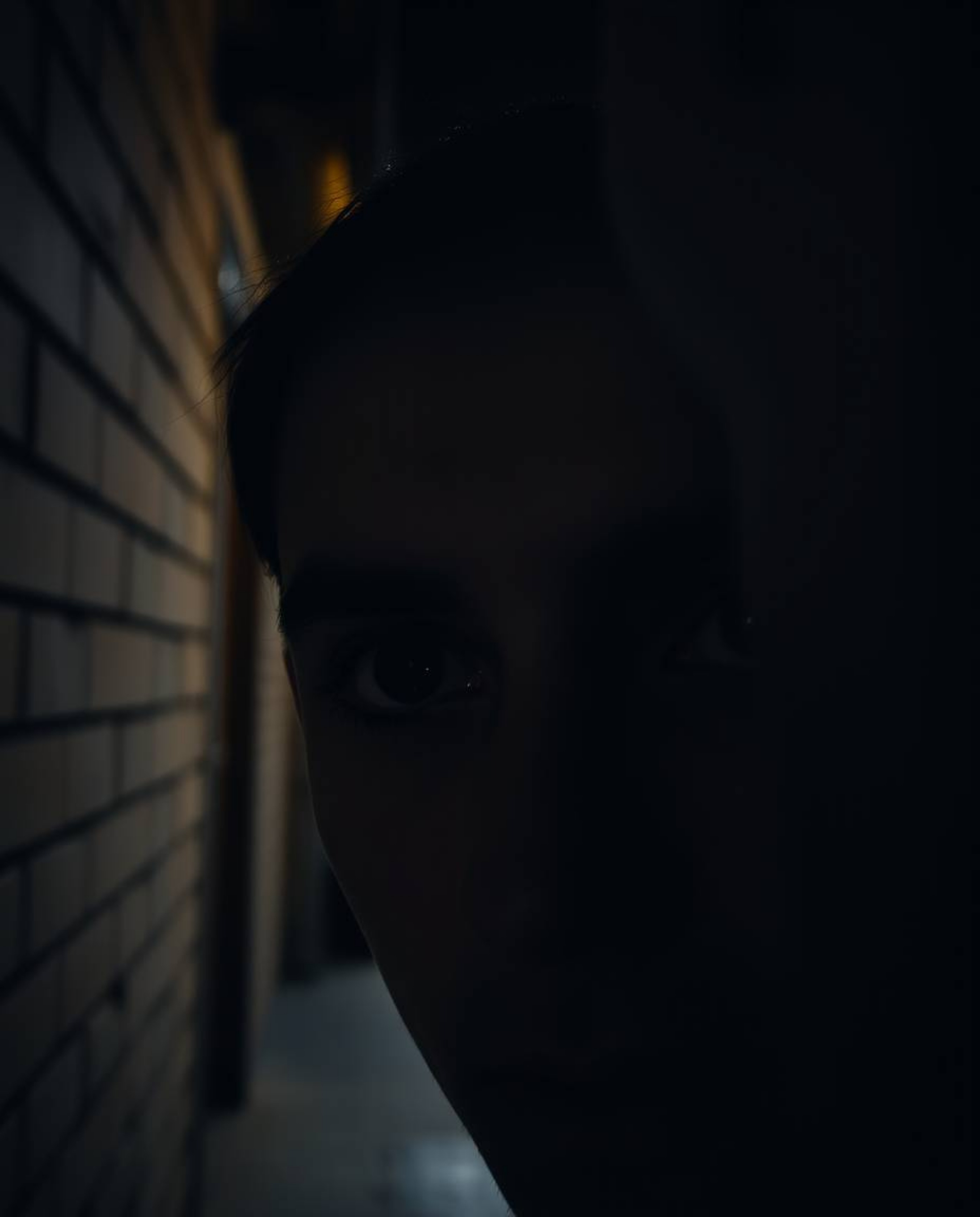 A captivating candid street photograph captures the intense gaze of jet-black eyes, piercing through the shadows of a dimly l