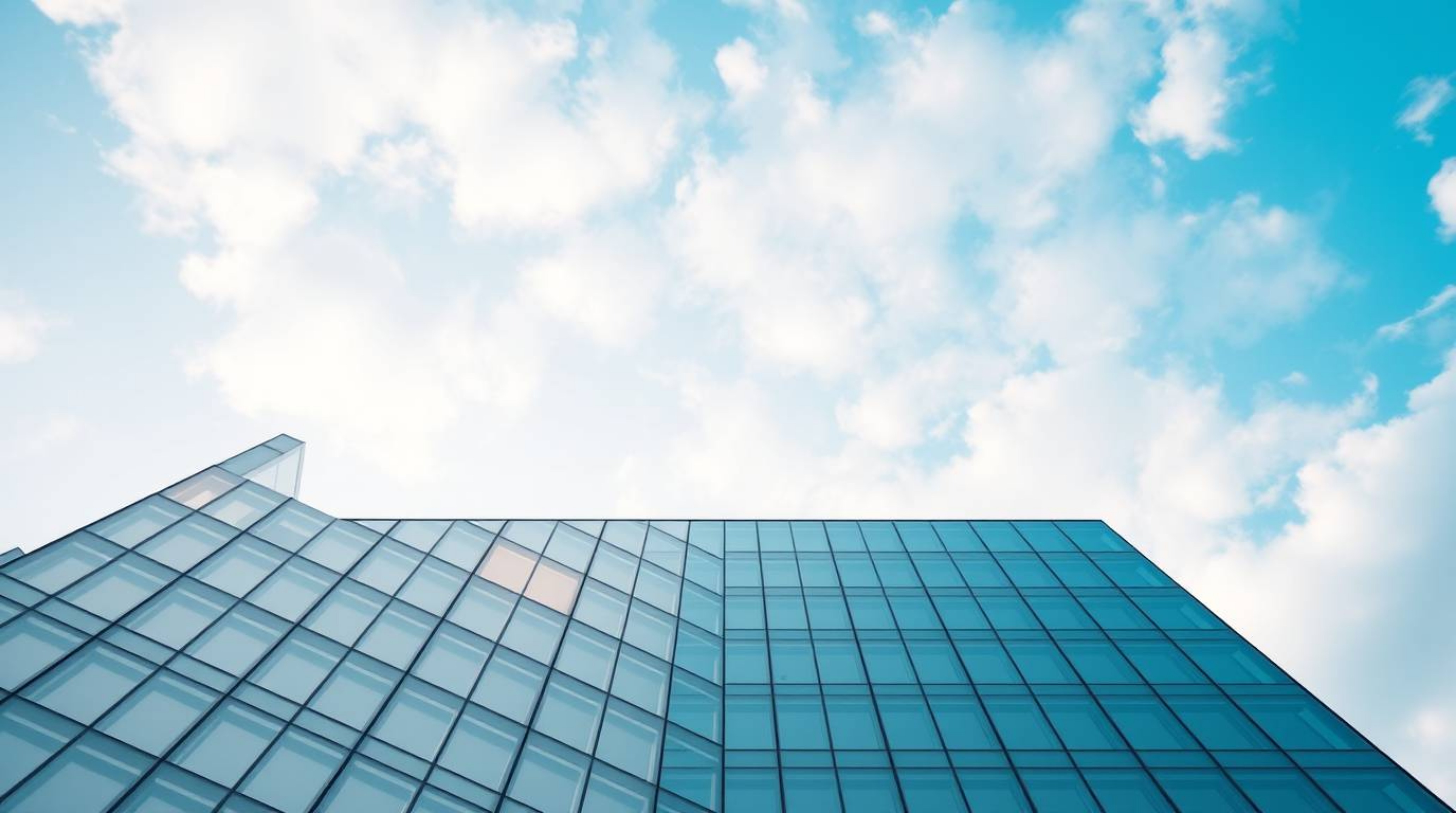 A precise architectural color photograph capturing a modern glass building seemingly dissolving into a soft, cloud-filled sky