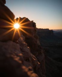 A close-up shot captures a sunset illuminating sandstone cliffs, employing dramatic chiaroscuro lighting. This technique crea