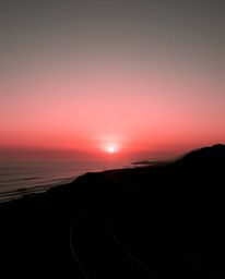 This is a graceful and elegant depiction of a sunset sky over a winding coastal highway. The artwork is rendered entirely in 