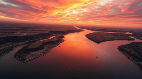 A stunning high-resolution image depicts a winding river glowing under a dramatic orange-pink sky, captured from a bird's-eye