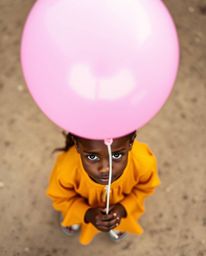 A captivating overhead shot captures a child with olive skin gently holding a vibrant balloon.  This fine art photograph, bat