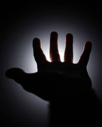 A captivating extreme macro photograph depicts a hand emerging from darkness towards a soft, warm light. This unusual, origin