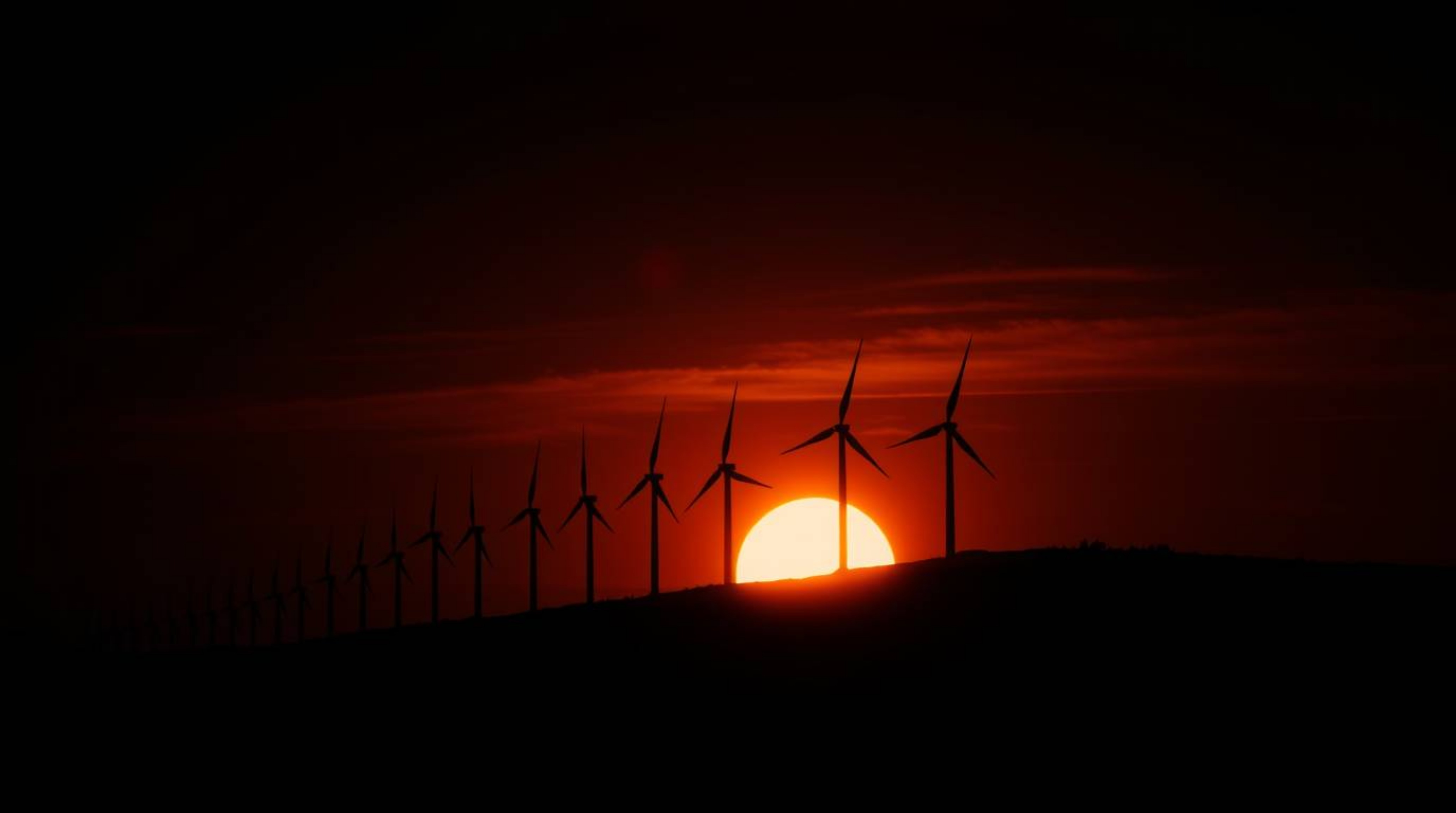 A dramatic cinematic scene featuring a sunset behind a row of wind turbines on a hill. The high contrast and low-key lighting