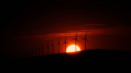 A dramatic cinematic scene featuring a sunset behind a row of wind turbines on a hill. The high contrast and low-key lighting