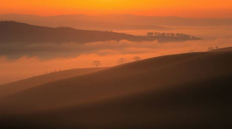 Capture the magic of golden hour with this stunning photograph of fog-covered hills bathed in soft, warm sunset light.  Reds,