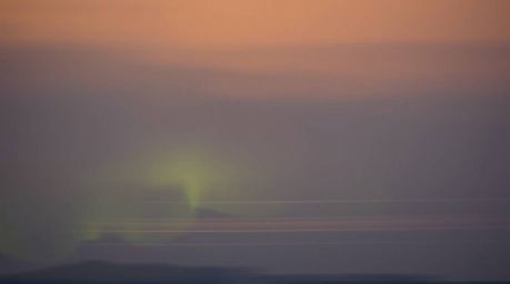 Capture the ethereal beauty of the Northern Lights emerging during a hazy sunset. This long-exposure photograph showcases sof