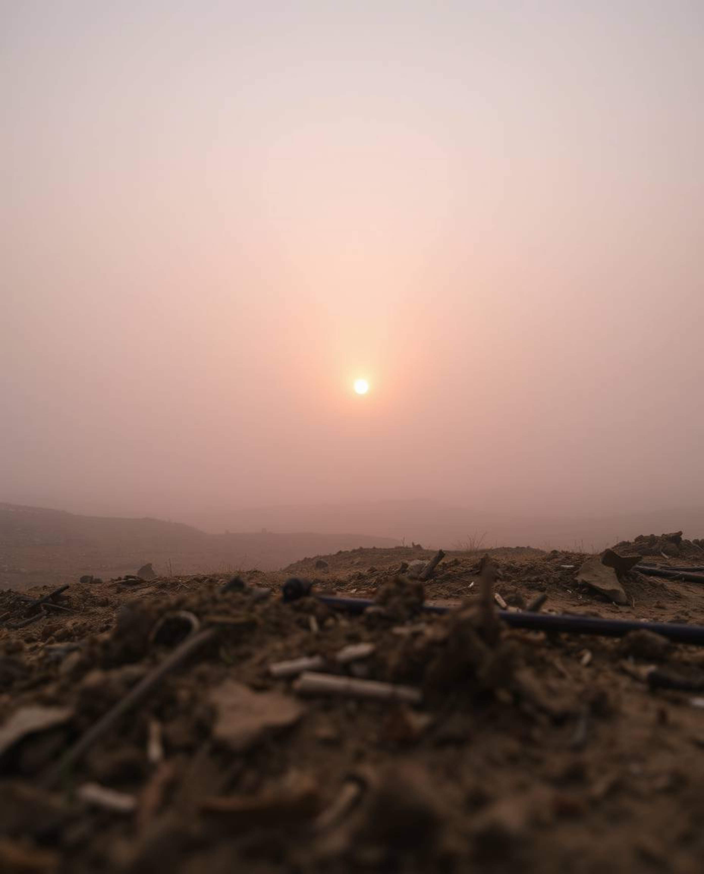 An extreme macro close-up shot capturing a sunrise over a war-torn landscape, characterized by thick fog, low visibility, and