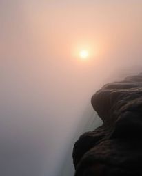 An extreme macro close-up captures a sun setting behind a dramatic waterfall amidst thick foggy surroundings. The scene is ch