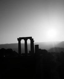 An overhead shot, presented as a classic black and white photograph, captures ancient stone ruins silhouetted against a sunse
