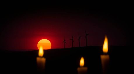 A captivating and moody image portrays a stunning sunset backdrop behind a row of wind turbines perched atop a hill. The scen