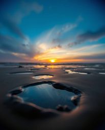 A photograph depicts a sunset sky mirrored in tidal pools on the beach. The scene is captured using strong, hard light which 