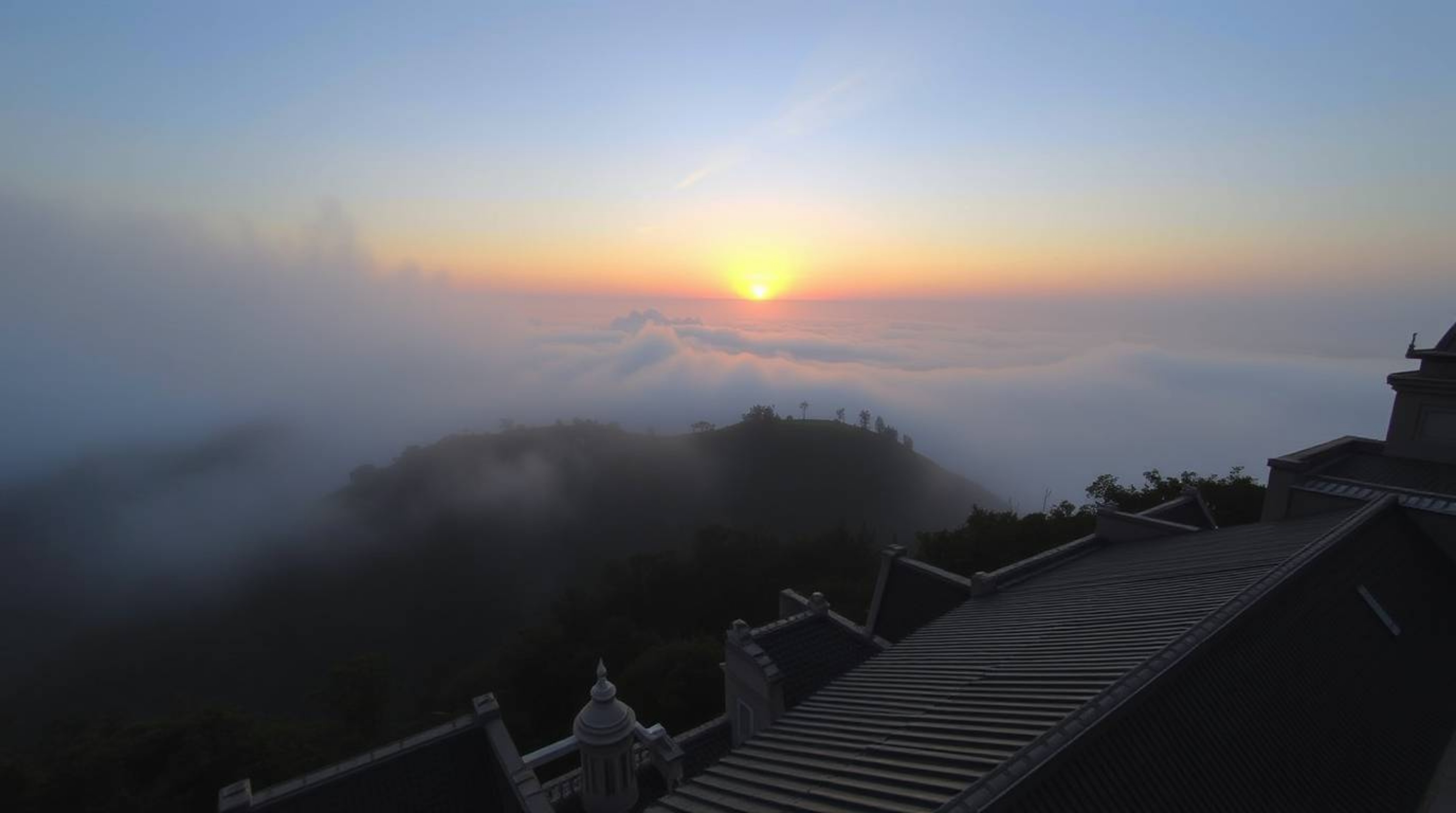 A stunning architectural photograph showcasing a wide-angle, top-down perspective of fog-shrouded hills bathed in the warm gl