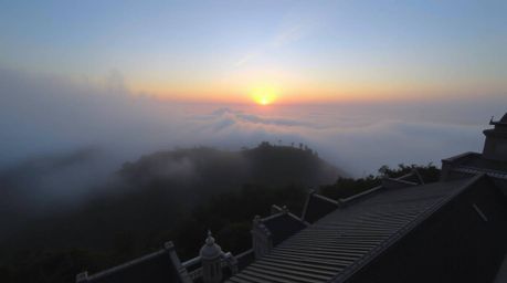 A stunning architectural photograph showcasing a wide-angle, top-down perspective of fog-shrouded hills bathed in the warm gl