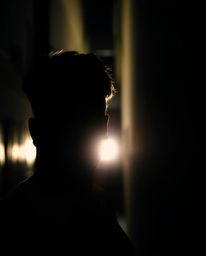 Eerie silhouetted eyes pierce through the darkness from a hidden alleyway at night. Backlighting creates an iridescent effect