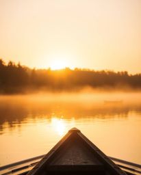 A boat is captured drifting on a lake at sunset, bathed in the beautiful, warm golden hour light. The scene is enveloped in a