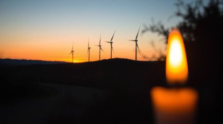 A captivating photograph captures a breathtaking sunset casting a warm glow behind a row of wind turbines perched atop a hill
