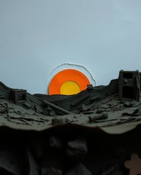 A dramatic, low-angle view of a sunrise over a war-torn landscape meticulously crafted from layered papier-mâché.  The textur