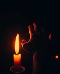 A captivating image depicts a hand emerging from darkness, reaching towards a warm, candlelit light.  The surreal scene is en
