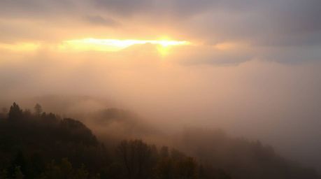 Experience the breathtaking beauty of fog-covered hills bathed in the warm glow of a breaking sunset. This captivating landsc