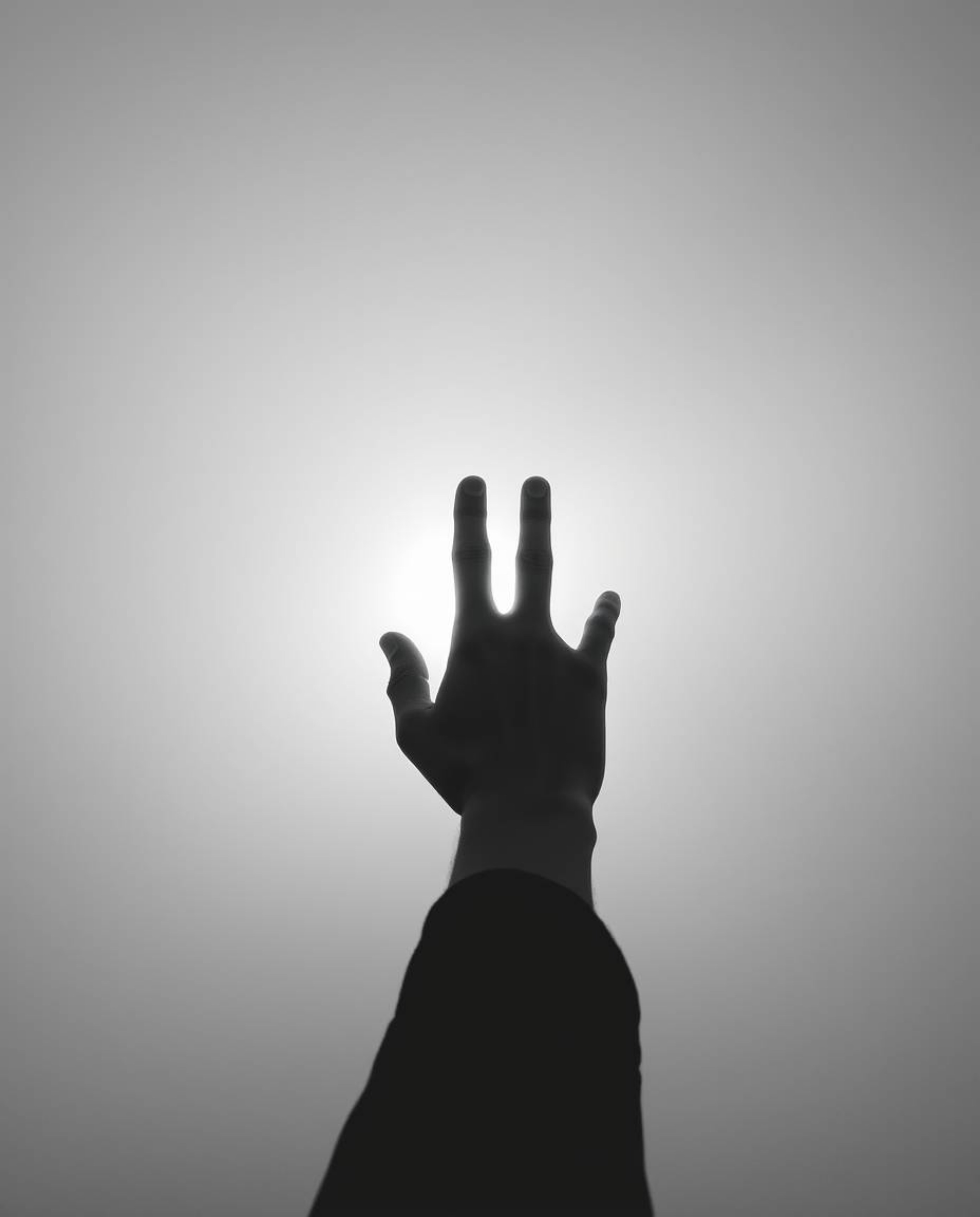 A captivating black and white photograph depicts a hand reaching towards a light source, emerging from a misty, obscured back
