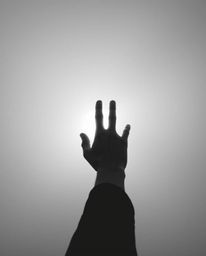 A captivating black and white photograph depicts a hand reaching towards a light source, emerging from a misty, obscured back