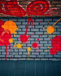 This image showcases vibrant graffiti-style splashes in warm tones of reds, oranges, and yellows adorning a textured brick wa