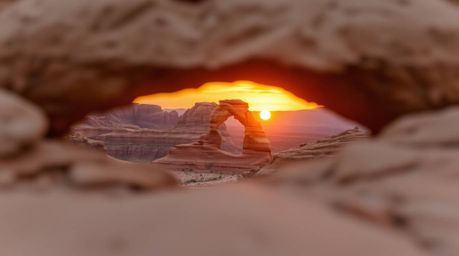 A stunning landscape photograph captures a vibrant desert sunset viewed through a natural rock arch. The image features a blu