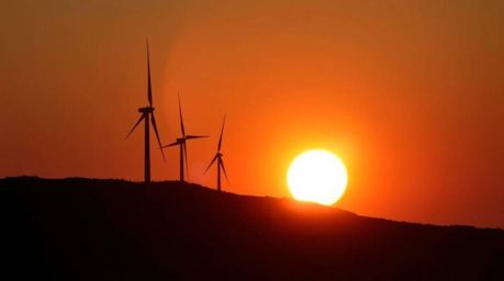 A stunning photograph capturing the beauty of a sunset behind wind turbines silhouetted against the bright light source on a 