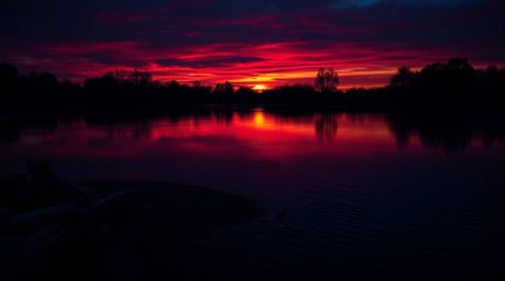 A captivating photograph showcases a serene pond mirroring a breathtaking sunset.  Rich burgundy and deep blue hues create a 