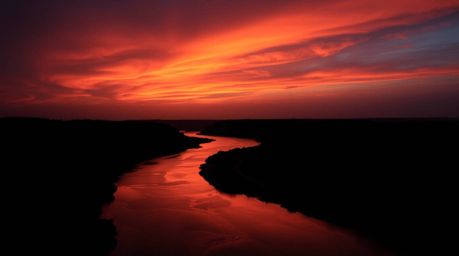 A high-resolution stock photo showcasing a winding river bathed in the dramatic glow of an orange-pink sky, achieved through 