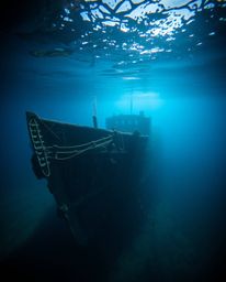 Discover a stunning high-resolution stock photo of a dramatically lit shipwreck deep underwater.  The image features strong, 