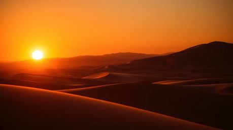 A captivating image showcases a graceful sunset at the edge of a desert, featuring golden dunes bathed in the warm glow of th