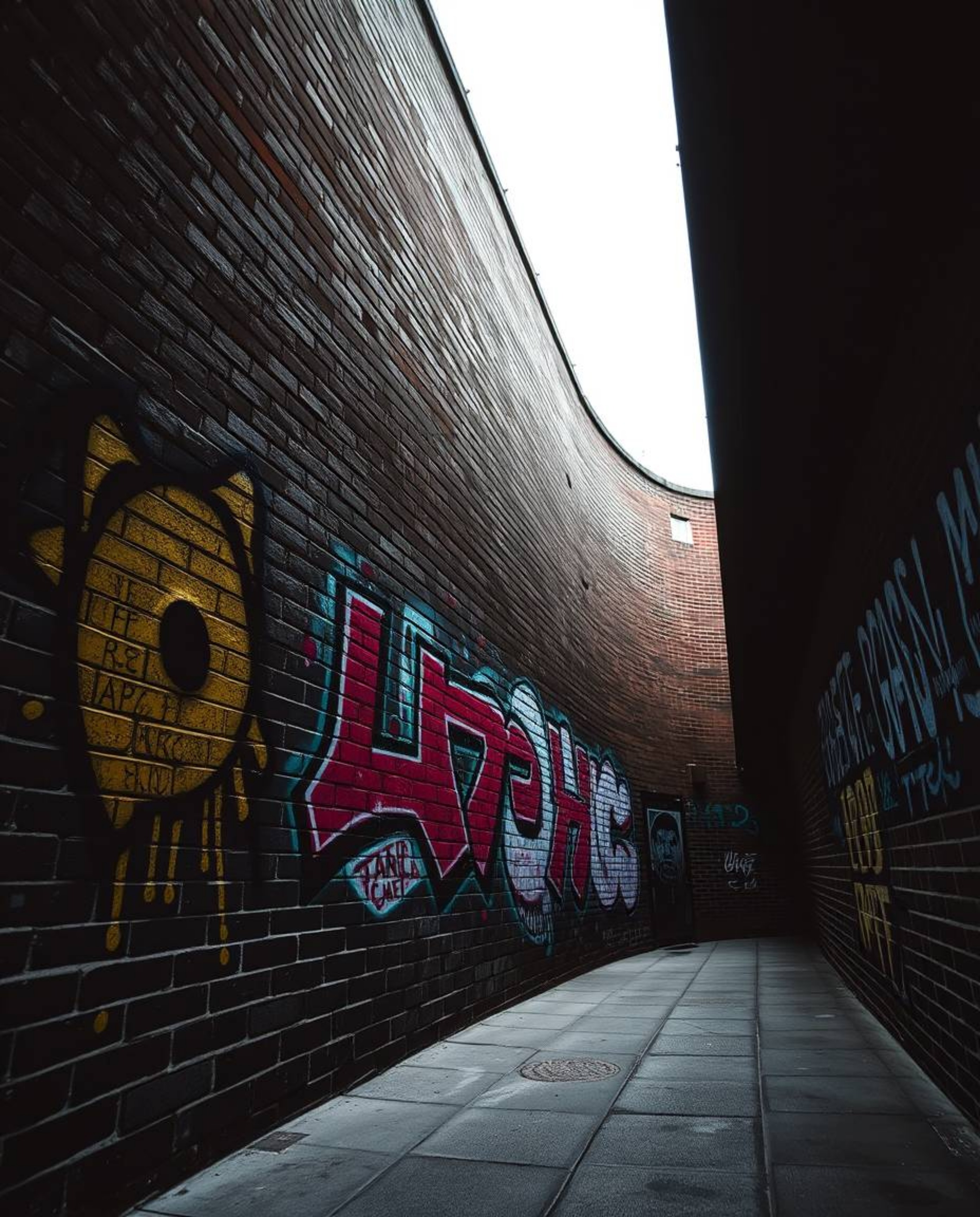 A striking high-contrast architectural photograph showcasing a brick wall adorned with vibrant graffiti-style splashes. The i