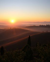 This is a high-resolution stock photo presenting a tight close-up of a sunset over the misty rolling hills of Tuscany. The im