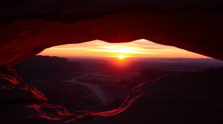 Experience the mesmerizing beauty of a desert sunset captured through a natural rock arch. This rich burgundy and deep blue c