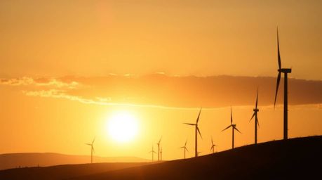 A captivating silhouette photograph captures the serene beauty of a sunset behind a row of wind turbines perched atop a hill.